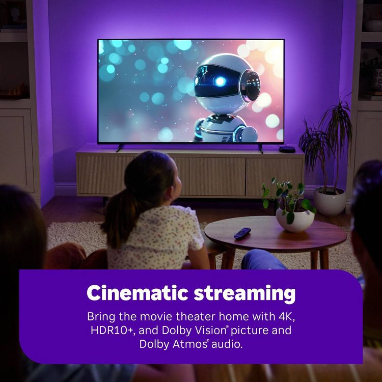 Roku Ultra – A large flat-screen TV displaying an animated robot is mounted on a wall with purple lighting, above a wooden console in a living room setting.
