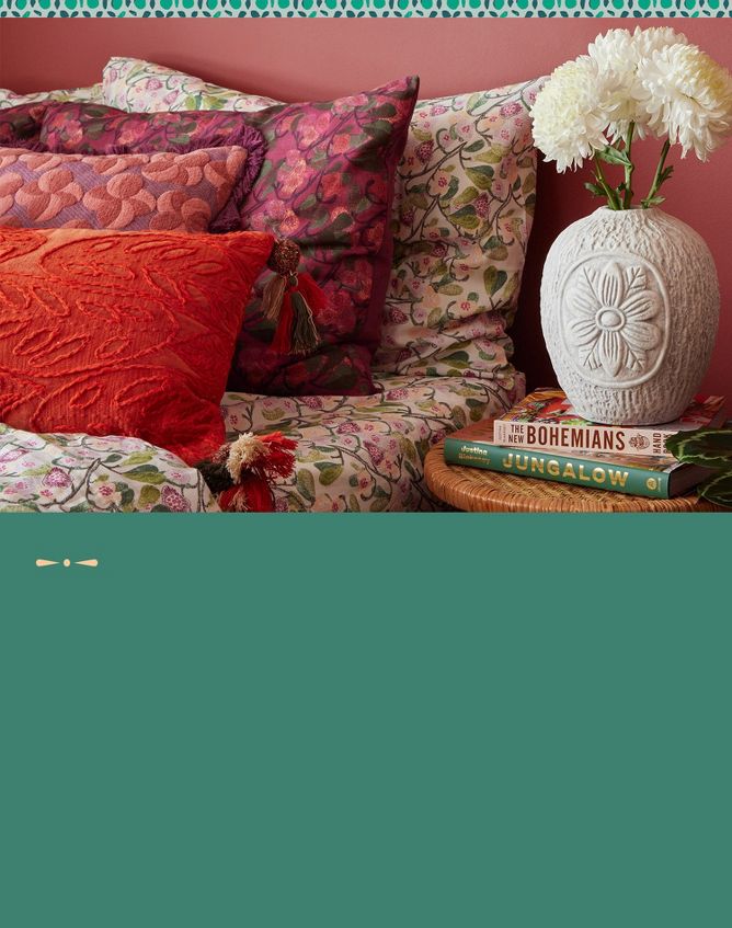 Colorful close-up shot of colorful patterned pillows on a bed beside a white textured floral vase holding white mums.