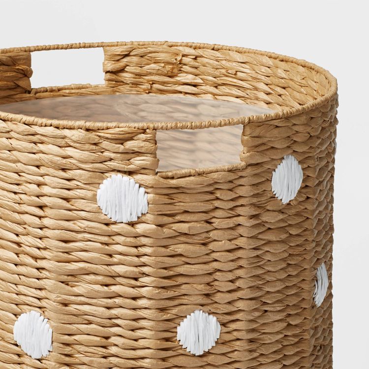A woven hamper with a natural colored finish and white colored polka dots, featuring cut-out handles.