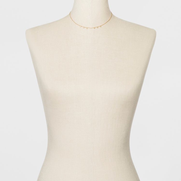 A delicate gold colored necklace with small dangling elements displayed on a mannequin.