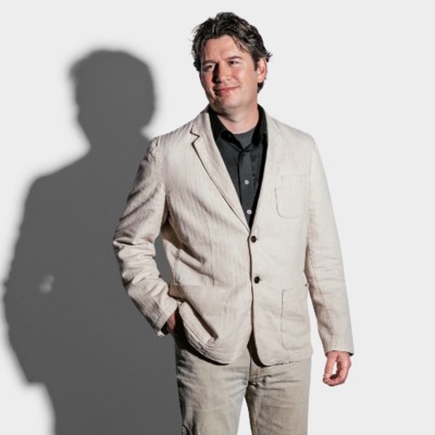 Profile Picture of Adam Nawrocki, A man with Mediterranean complexion, with brown curly hair, hair, wearing a black shirt with linen sport coat. 