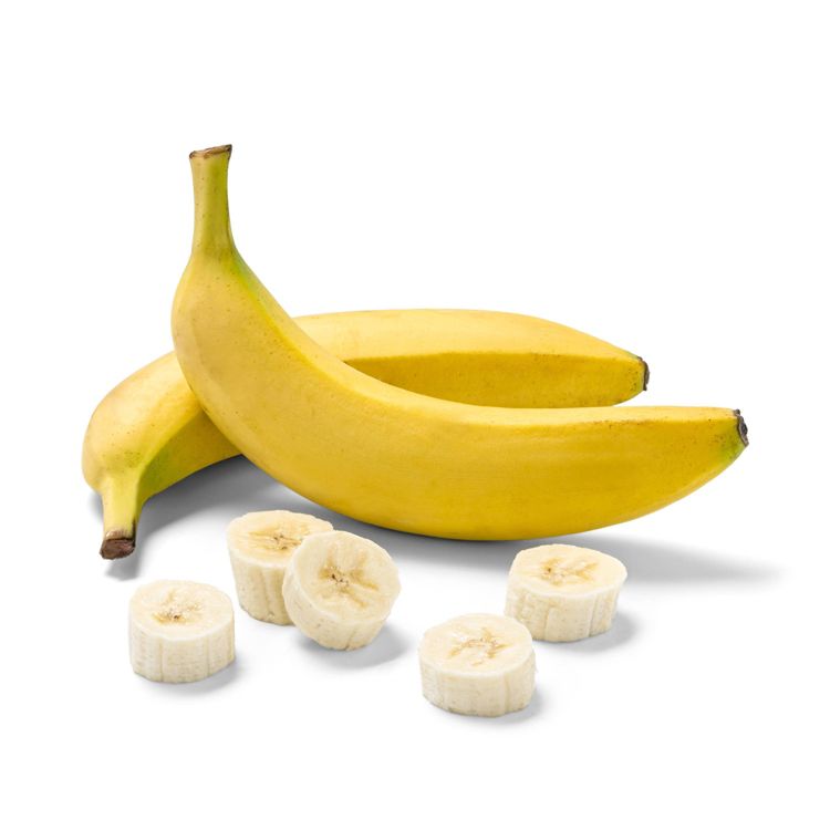 Two whole yellow colored bananas and several banana slices are arranged on a white surface.