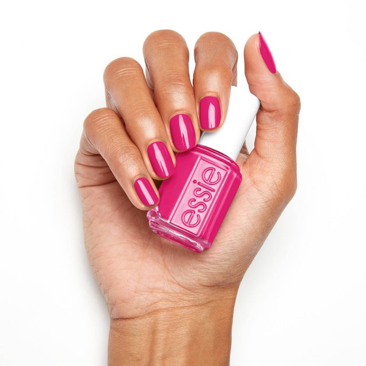 A hand holding a bottle of pink colored nail polish with matching pink colored nails.