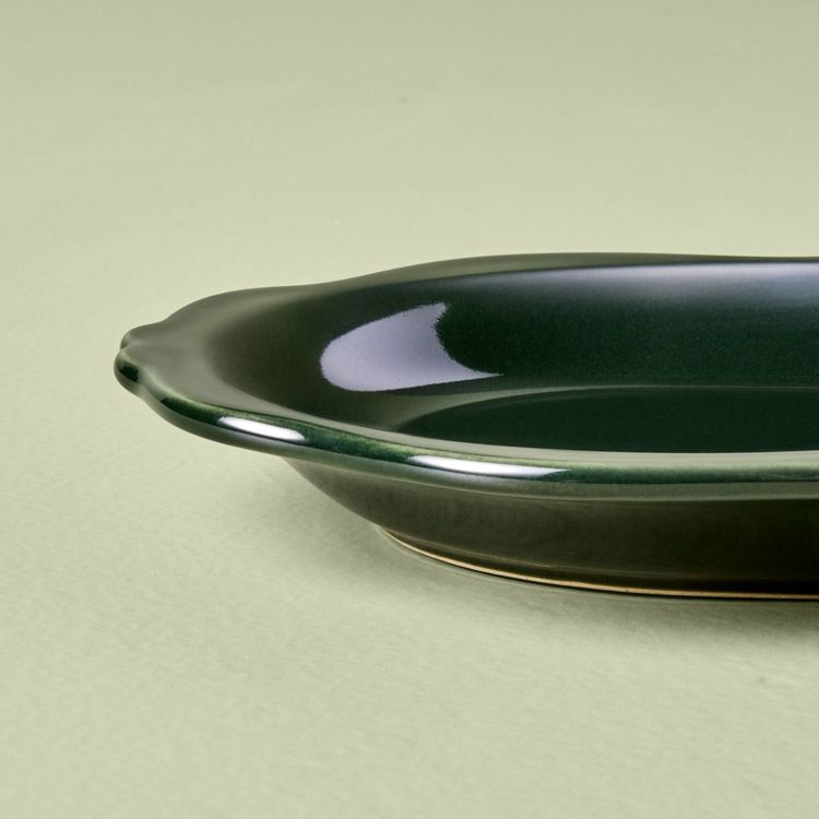 A dark green colored oval tray with a glossy finish on a light green surface.