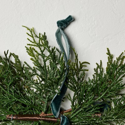 Greenery swag with a teal colored ribbon tied at the top against a white textured background.