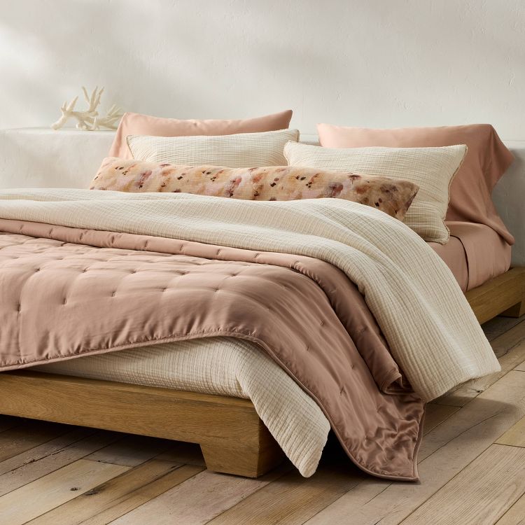 Natural-colored textured chambray comforter and sham set on a wooden bed, with layered pillows in beige and floral patterns.
