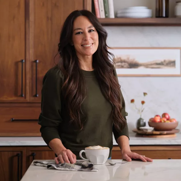 An image of Joanna gaines smiling in a kitchen, and a second photo of a knit blanket and cappuccino and cookies on a tray set on top of an ottoman.