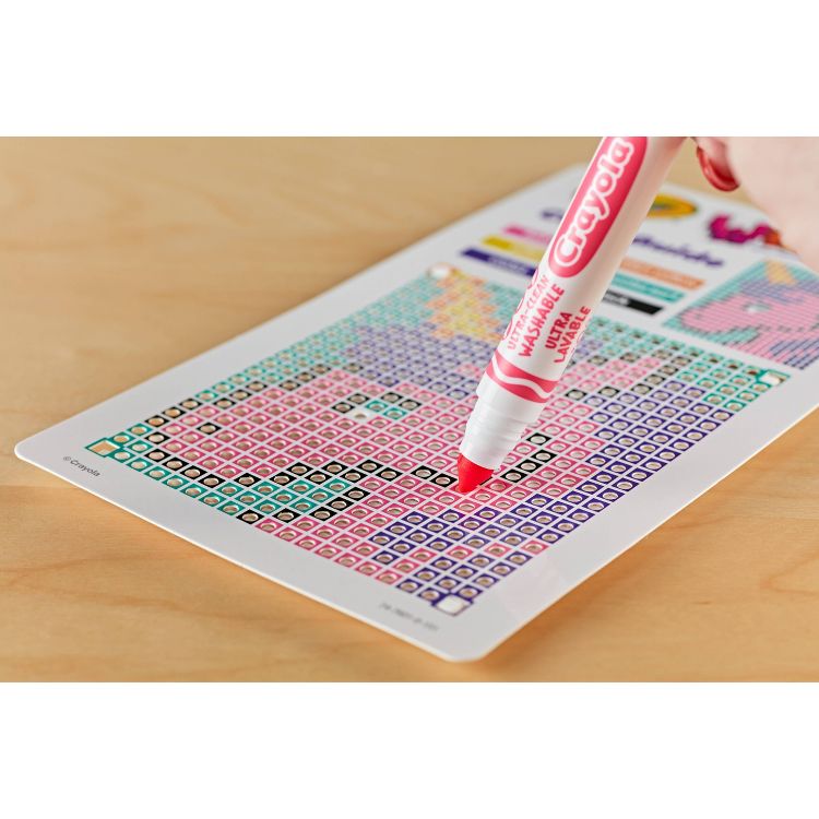 A red colored Crayola marker is being used to color a grid of small squares on a paper.