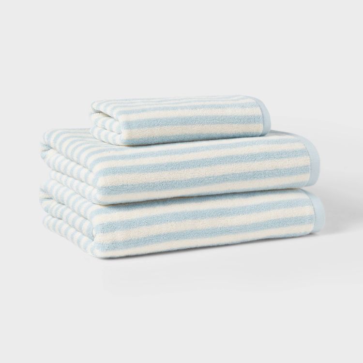 A stack of three light blue and white striped towels on a white surface.