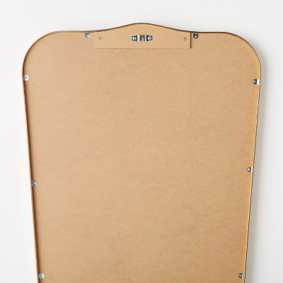 The back of a decorative wall mirror with a light brown colored backing and metal hanging hardware.