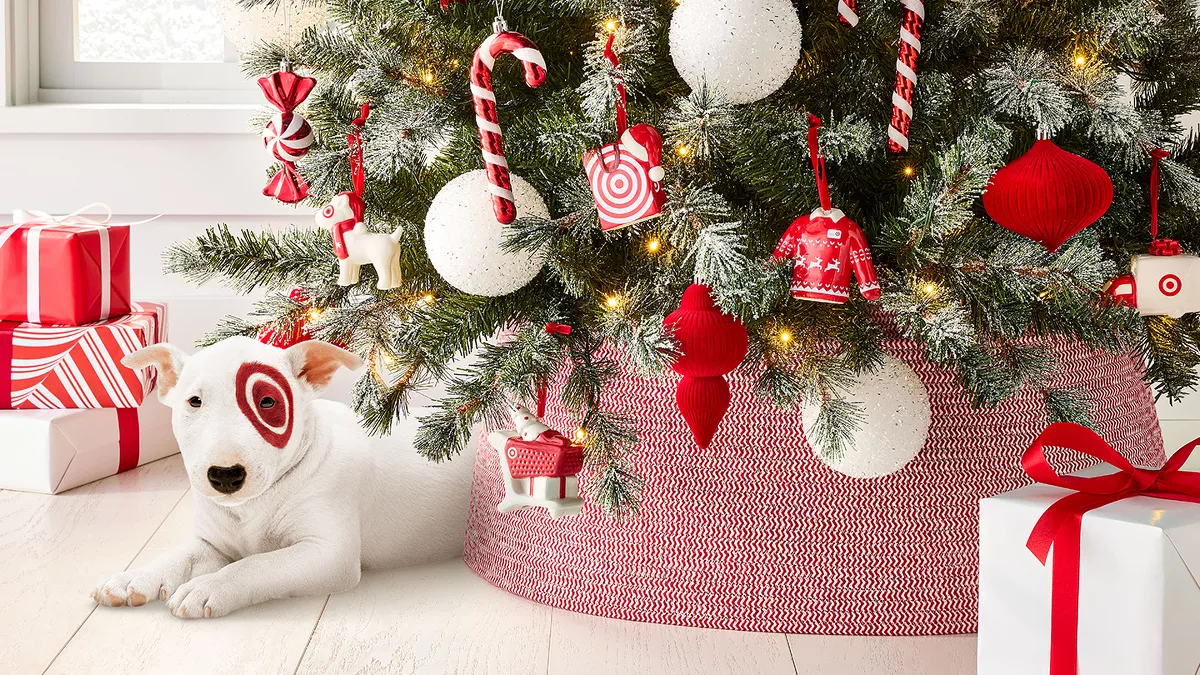 A festive Christmas tree with red, white, and candy cane decorations. Wrapped presents with red ribbons are beneath the tree. A cute, white dog with a red circle around one eye is lying on the floor, next to the tree. Warm lights twinkle on the tree.