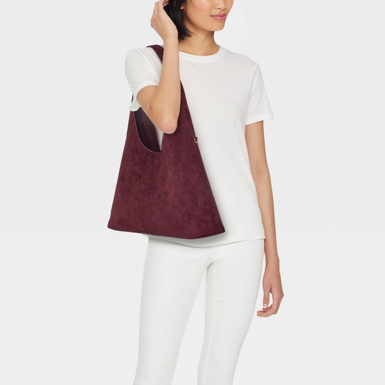 A person is holding a large, burgundy colored shoulder bag against a white background.