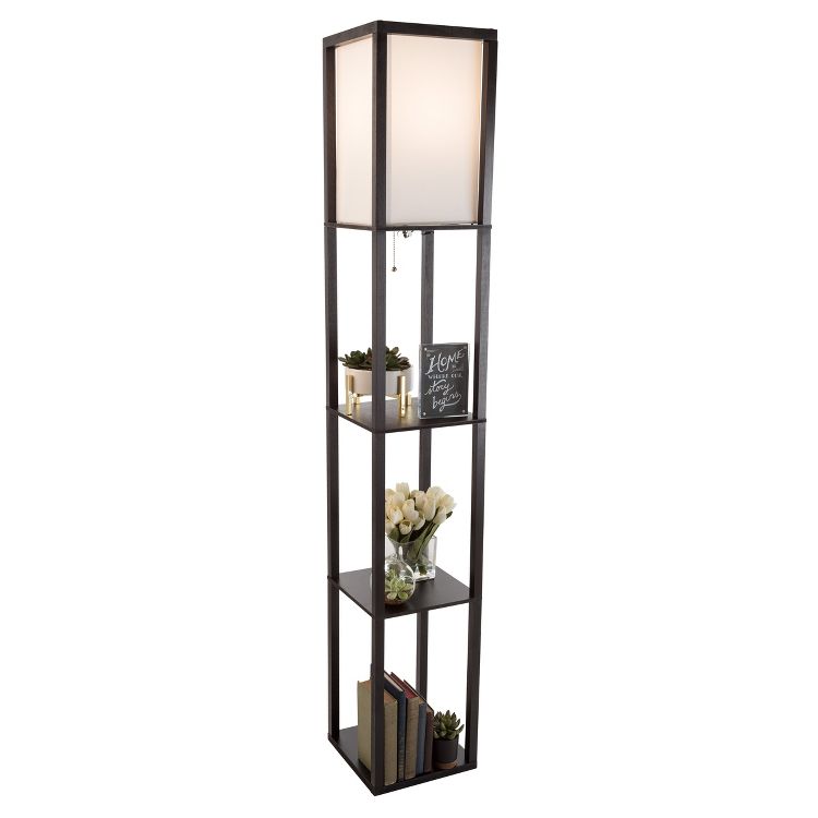 Tall floor lamp with a white colored shade and three shelves holding books, plants, and a small sign.