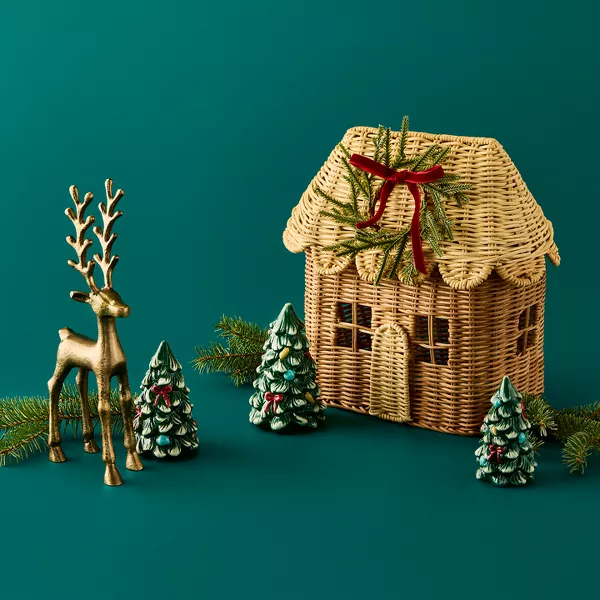 A festive collage of holiday decor, including a greenery wreath, tree-shaped candles, gold reindeer, embroidered pillows, a wicker house and ceramic trees.