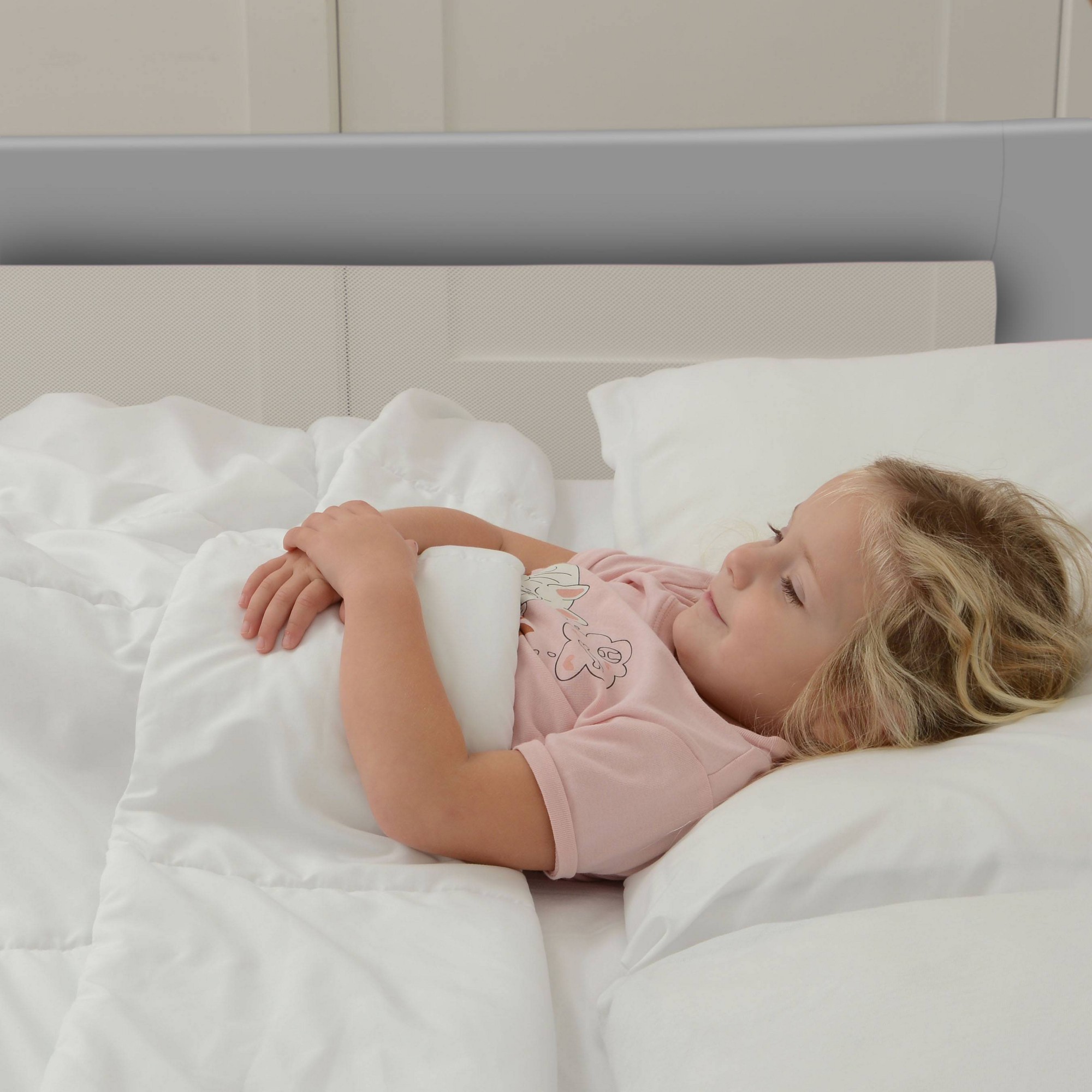 A young girl resting her arms on a gray bed rail.
