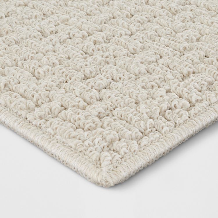 A close-up of a beige colored rug with a textured looped pattern and finished edges.