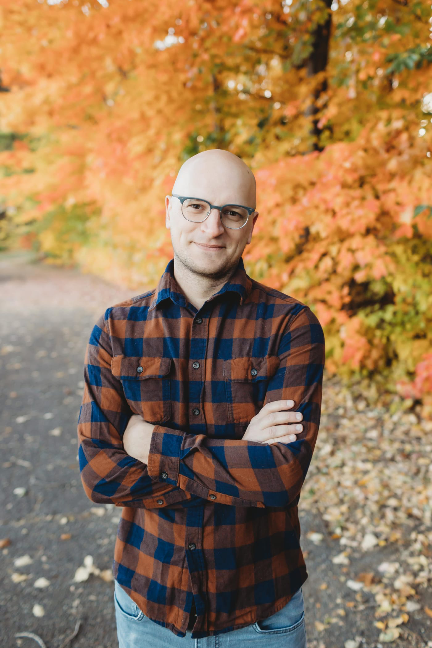 Target Principal Engineer Brian Muenzenmeyer, a man with light skin, wearing glasses and a button down flannel shirt and smiling with his arms crossed against a background of colorful fall leaves