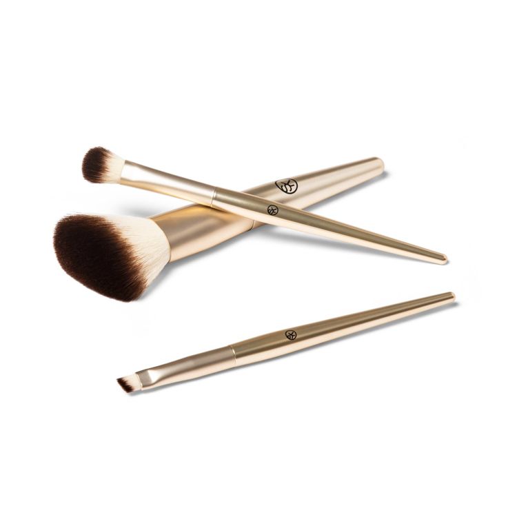 Three gold colored makeup brushes with different brush head shapes are arranged on a white background.