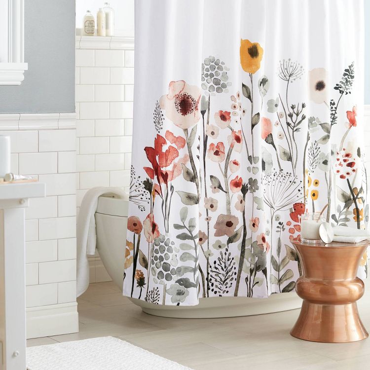 A white colored shower curtain with a floral pattern in red, orange, and green hues hanging in a bathroom.