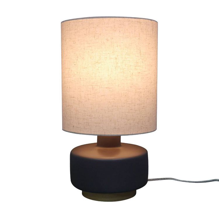 A table lamp with a cylindrical beige colored shade and a round dark base.
