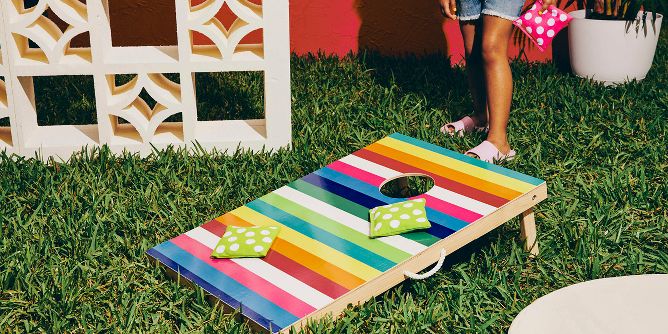 Girl playing bean bag toss with colorful, multi-stripe game boards and polka dot bean bags in bright pink and lime green.
