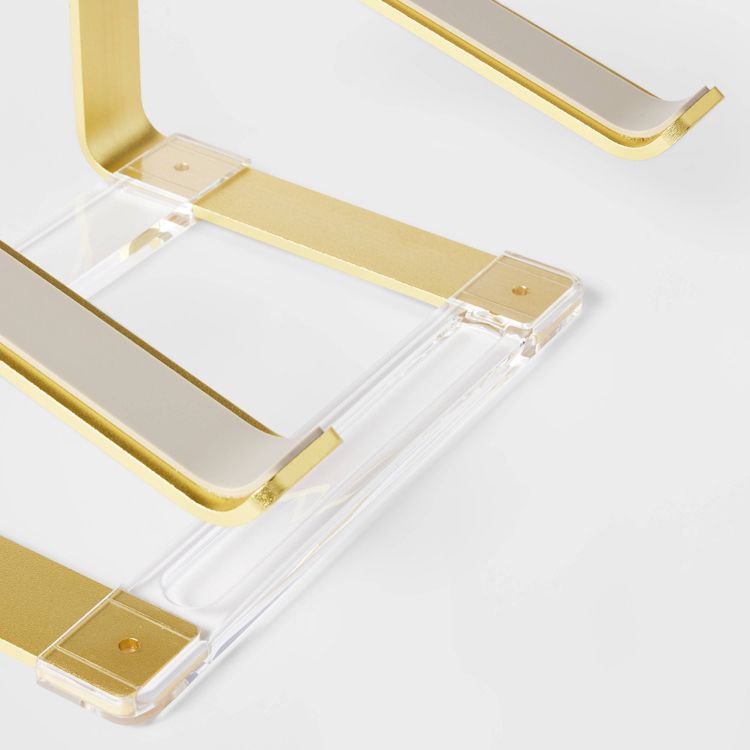 A gold colored and clear acrylic riser with a rectangular base and curved edges.