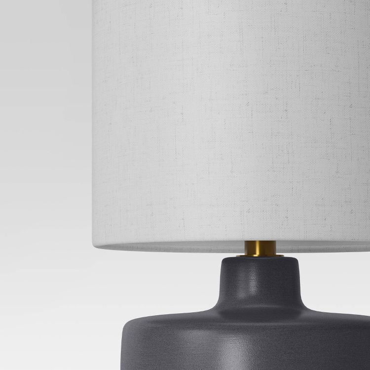 A close-up of a lamp with a white colored fabric shade and a dark gray colored base.