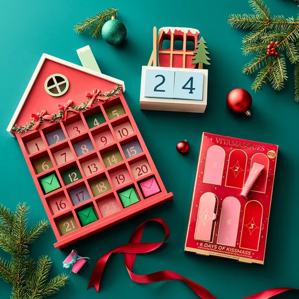 Holiday advent calendars arranged with evergreen branches, ornaments and red ribbon on a teal background.
