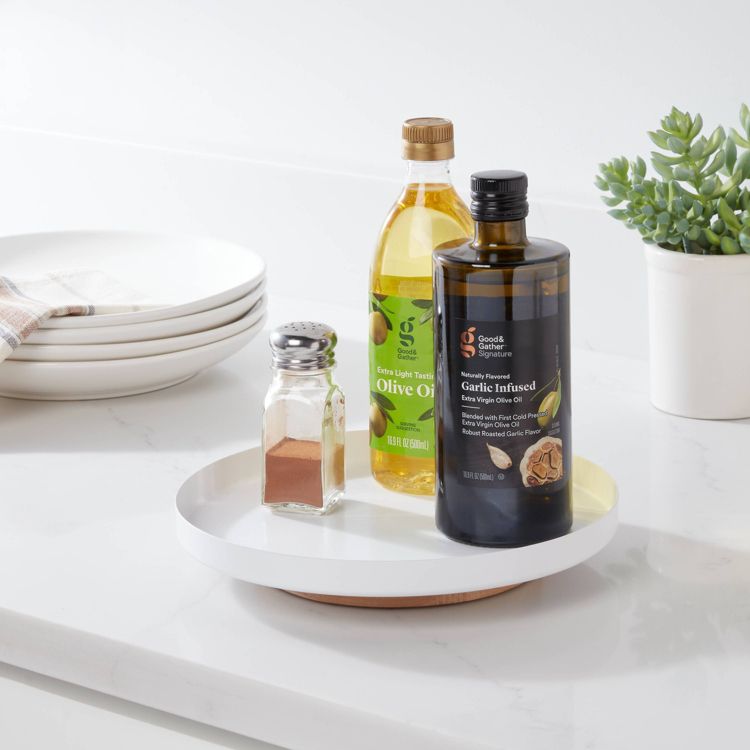A white round organizer holding a bottle of olive oil, a bottle of garlic infused olive oil, and a small glass spice shaker on a kitchen counter.