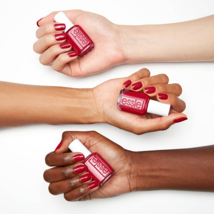 Three hands holding bottles of red colored nail polish with matching painted nails, each bottle labeled "essie."