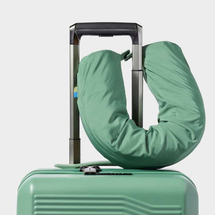 A green colored neck pillow attached to the handle of a matching green suitcase.