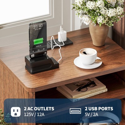 Wooden nightstand with a smartphone dock, a cup of coffee, a vase of flowers, and books on the lower shelf, featuring 2 AC outlets and 2 USB ports.