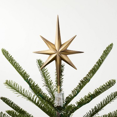 A gold colored star-shaped tree topper placed on the top of a Christmas tree.