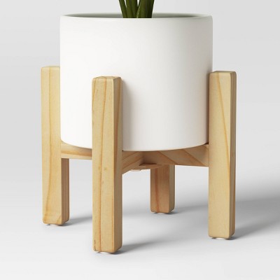 A white colored cylindrical planter is placed on a light wooden stand.