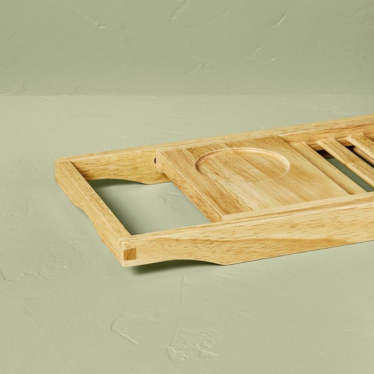 A light brown colored wooden tray with a circular indentation and slatted sections, placed on a light green surface.