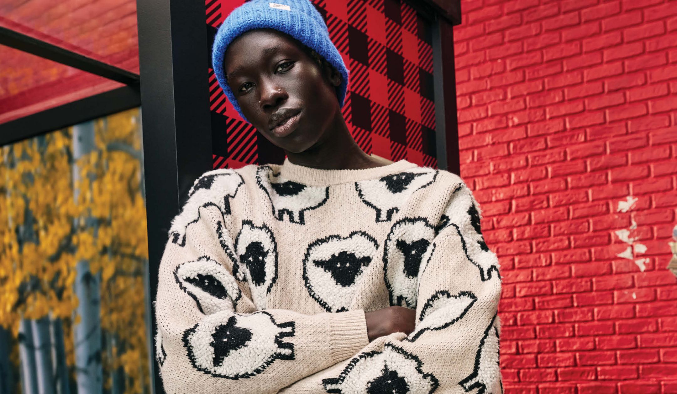 image features a man in an all-over graphic sheep sweater with black cargo pants & a blue beanie.