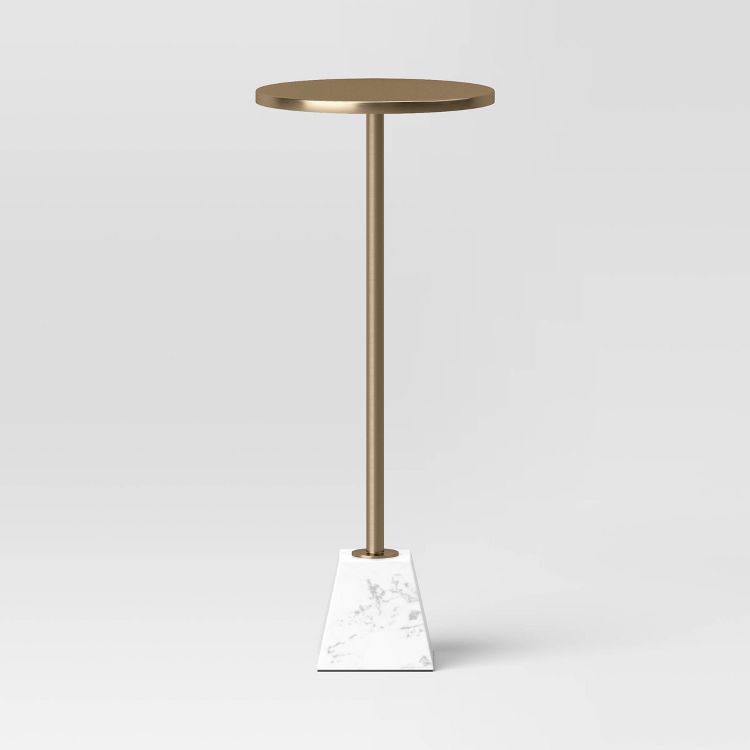 A round, gold colored end table with a slender stand and a white, pyramid-shaped base.