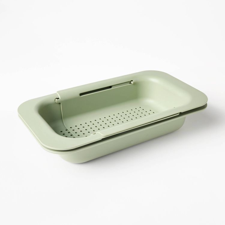 A light green colored rectangular colander with a perforated base and extendable handles.