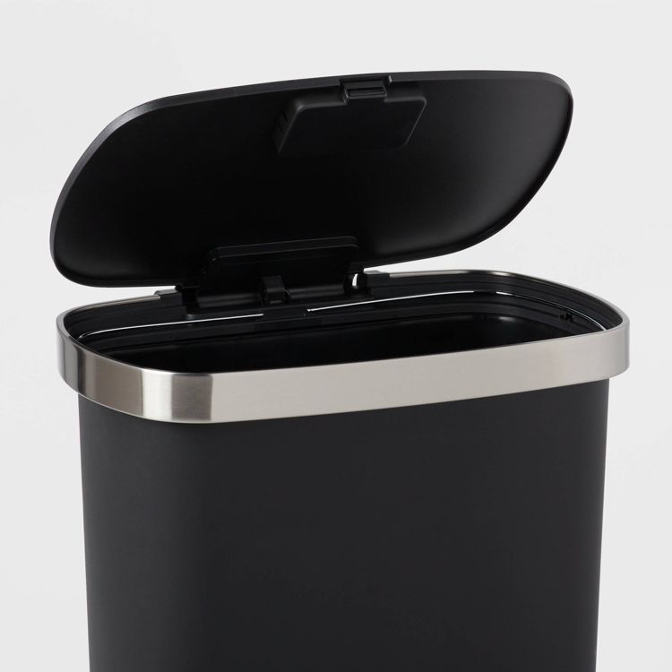 A black colored indoor trash can with an open lid and a silver colored rim.