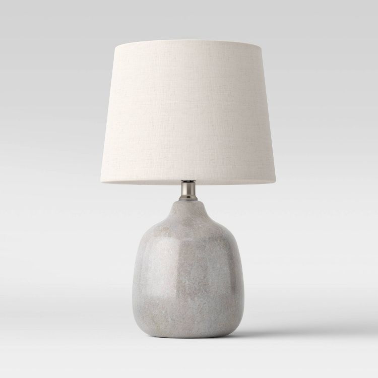 A table lamp with a light gray colored ceramic base and a white colored fabric shade.
