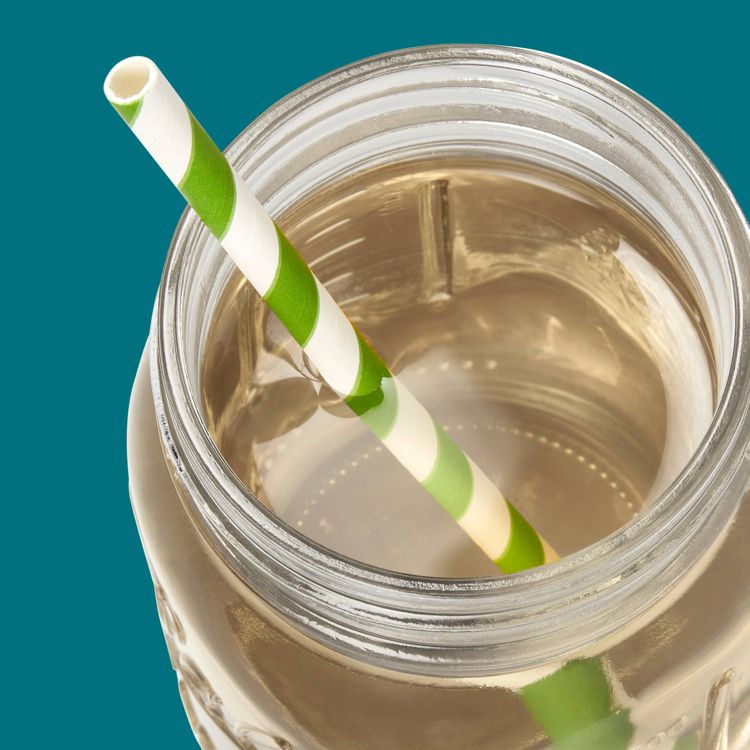 A clear glass jar filled with liquid and a green and white striped straw inside.