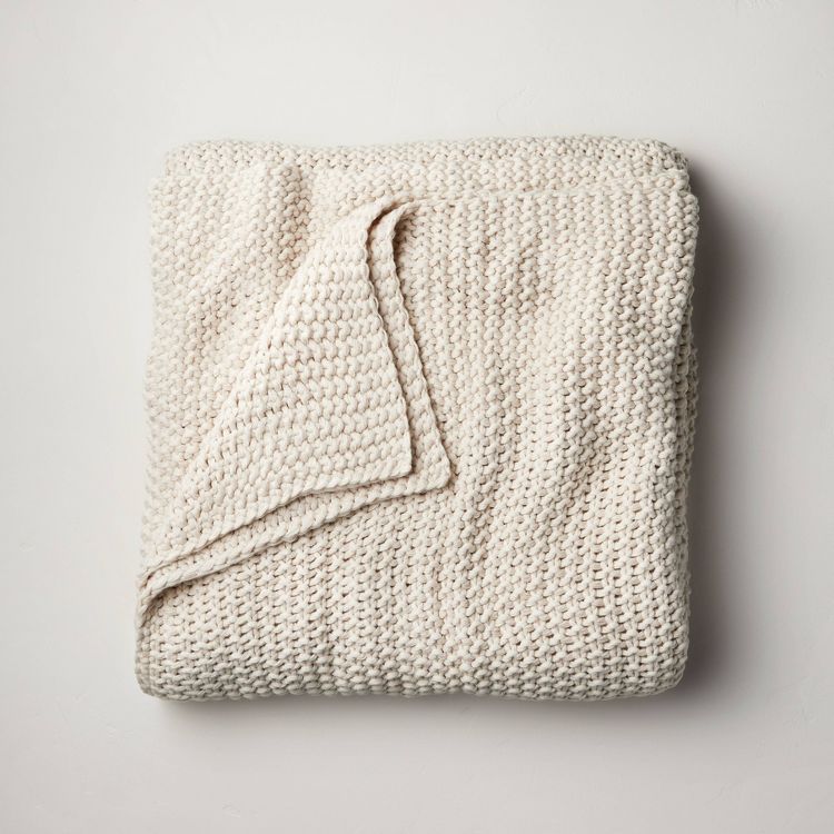 Chunky knit bed blanket in a natural color, folded neatly with a visible textured pattern.