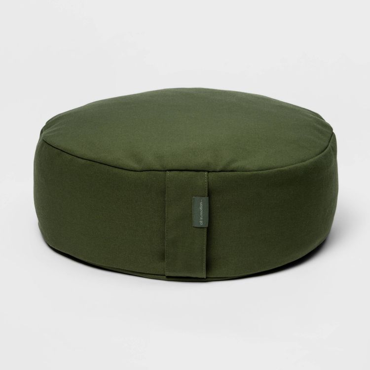 Round, dark green colored pillow with a small fabric tag on the side.