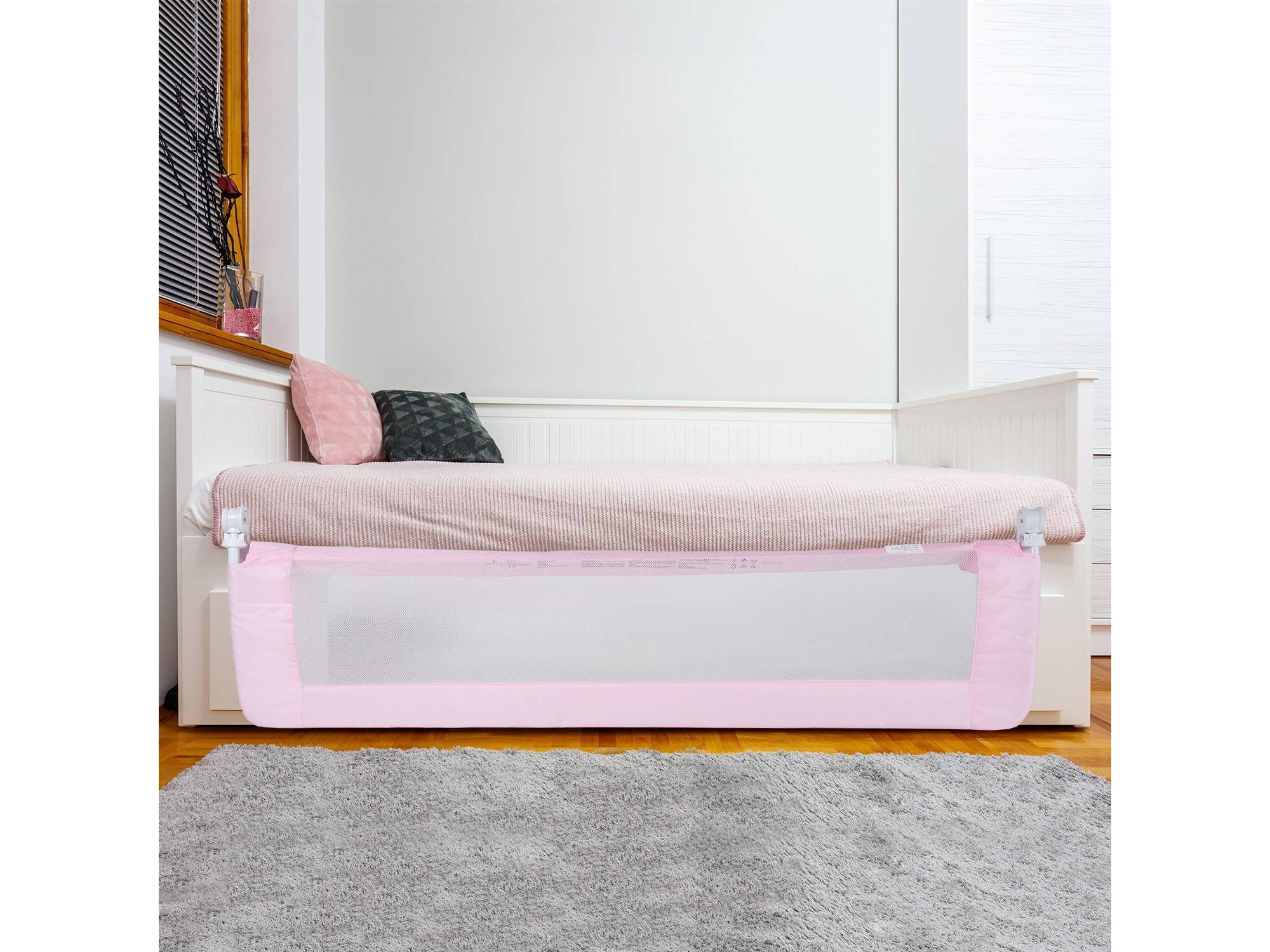 A pink bed rail with a white mesh panel on a bed.