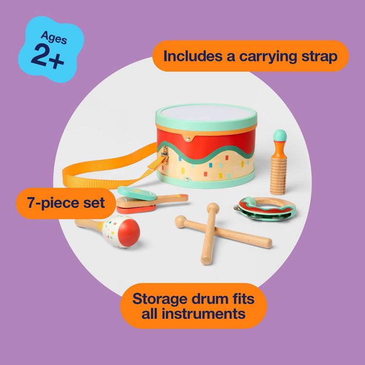 A colorful 7-piece children's instrument set with a drum, maracas, tambourine, and drumsticks, featuring a carrying strap and storage drum, labeled for ages 2+.