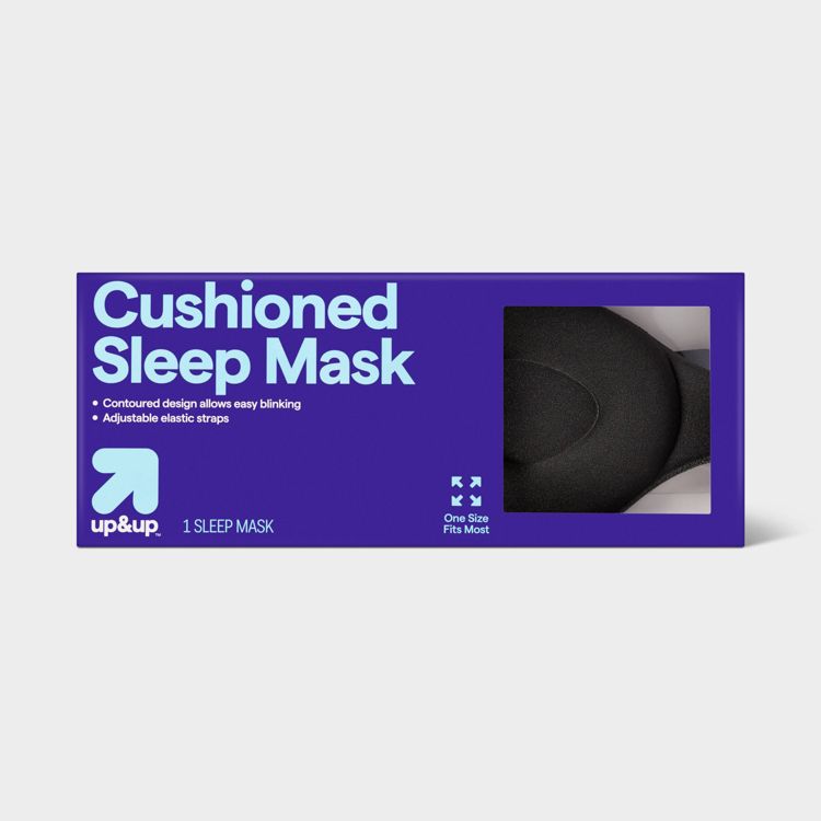 A black colored cushioned sleep mask in a purple box labeled "Cushioned Sleep Mask" with features like contoured design and adjustable elastic straps.