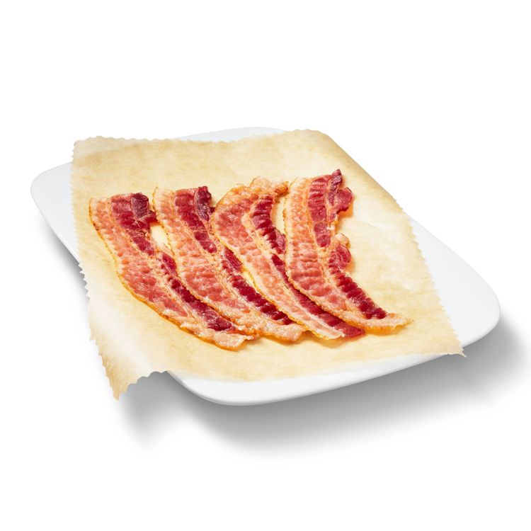 Crispy bacon strips placed on parchment paper on a white plate.