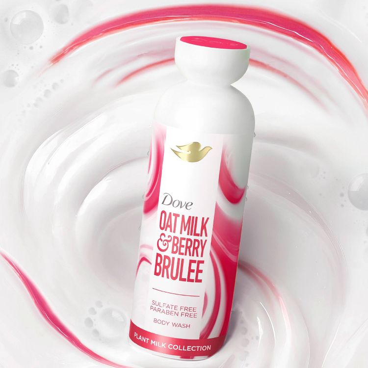 Dove Oat Milk & Berry Brulee Body Wash in a sleek, white bottle with pink swirls and a gold Dove logo. The background features a creamy, swirling mixture of white and pink, evoking a luxurious, moisturizing feel. Sulfate and paraben-free. 
