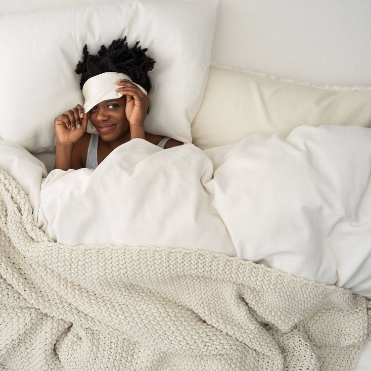 A cream colored knitted blanket is draped over white bedding.