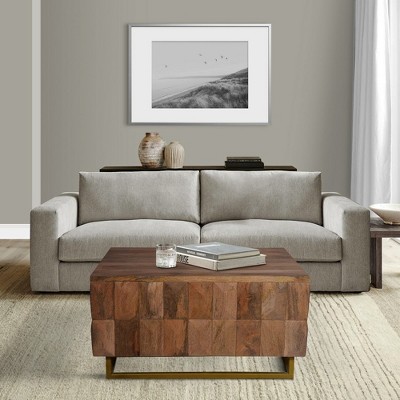 Square wooden block coffee table with brass base in front of a sofa